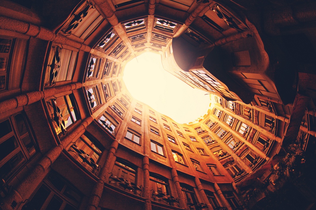 Bérház ovális udvarán az égre irányított kamerával készült fénykép, ahol a fény fokozatosan elmossa a magasabb emeletek ablakait